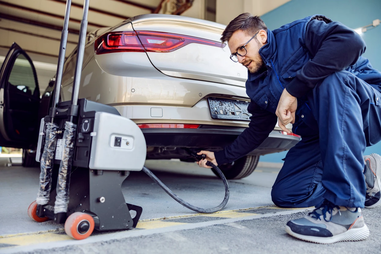 Mécanicien automobile en combinaison bleue effectuant un contrôle technique sur véhicule surélevé dans garage professionnel