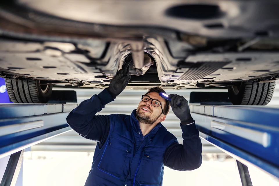 Mécanicien automobile travaillant sous un véhicule surélevé dans un garage professionnel