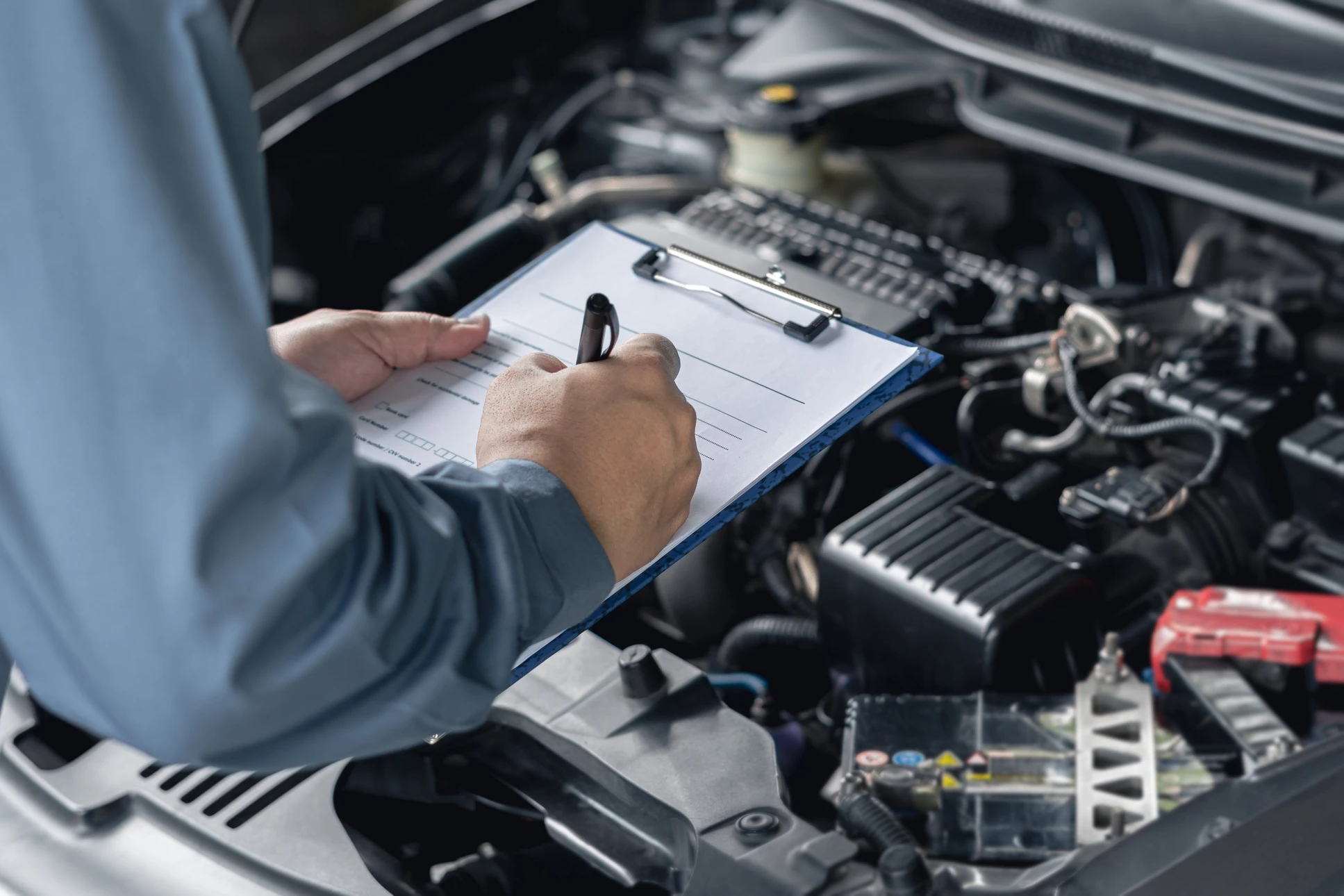Mécanicien automobile en combinaison travaillant sous un véhicule surélevé, portant des gants orange nitrile, manipulant un disque de frein