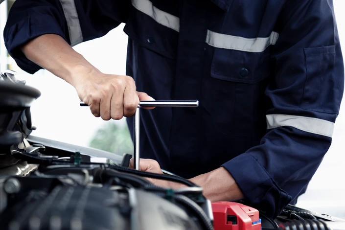 Mécanicien automobile en combinaison bleue effectuant un contrôle technique sur véhicule surélevé dans garage professionnel