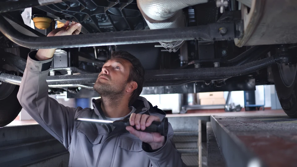 Mécanicien automobile en combinaison bleue inspectant une roue sur pont élévateur hydraulique dans garage professionnel